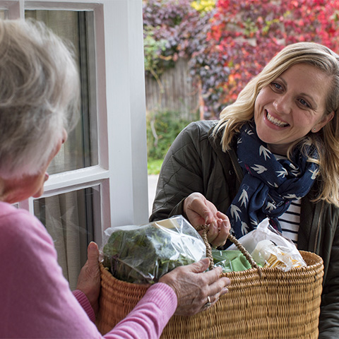 A middle-aged blond woman offering a welcome basket to a new neighbor.